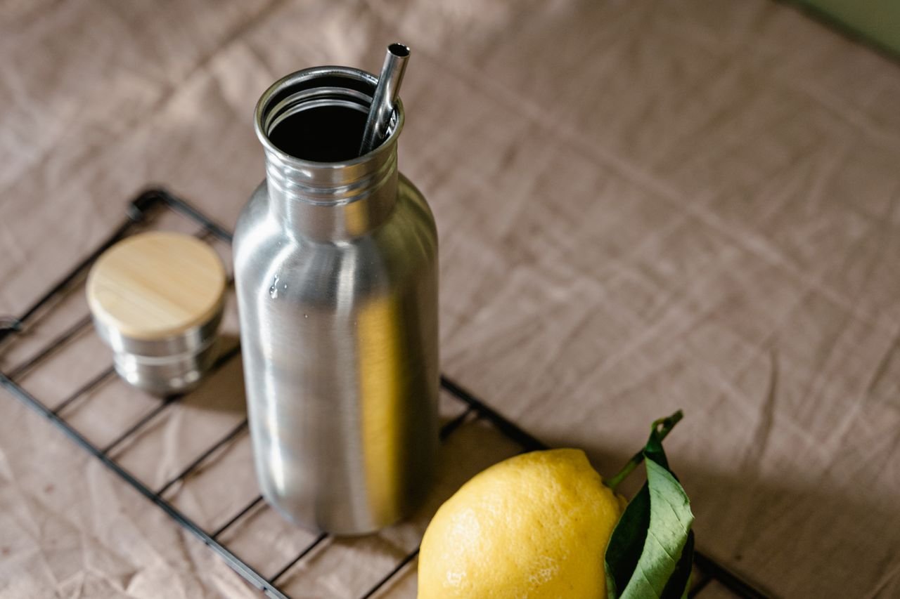 Eco-friendly metal bottle with lemon and reusable straw on natural fabric.